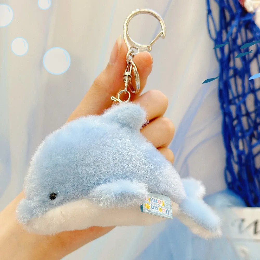 A light blue plush bunny keychain with soft fur and a gold ring being held by a hand.