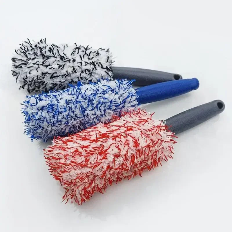 Trois brosses de nettoyage avec poignées noires et poils gris, bleu et rouge.