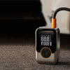 A silver wireless portable tire inflator with an orange nozzle and a digital display is shown on a dark surface.
