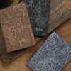 A stack of personalized leopard print passport holders in brown and gray tones.