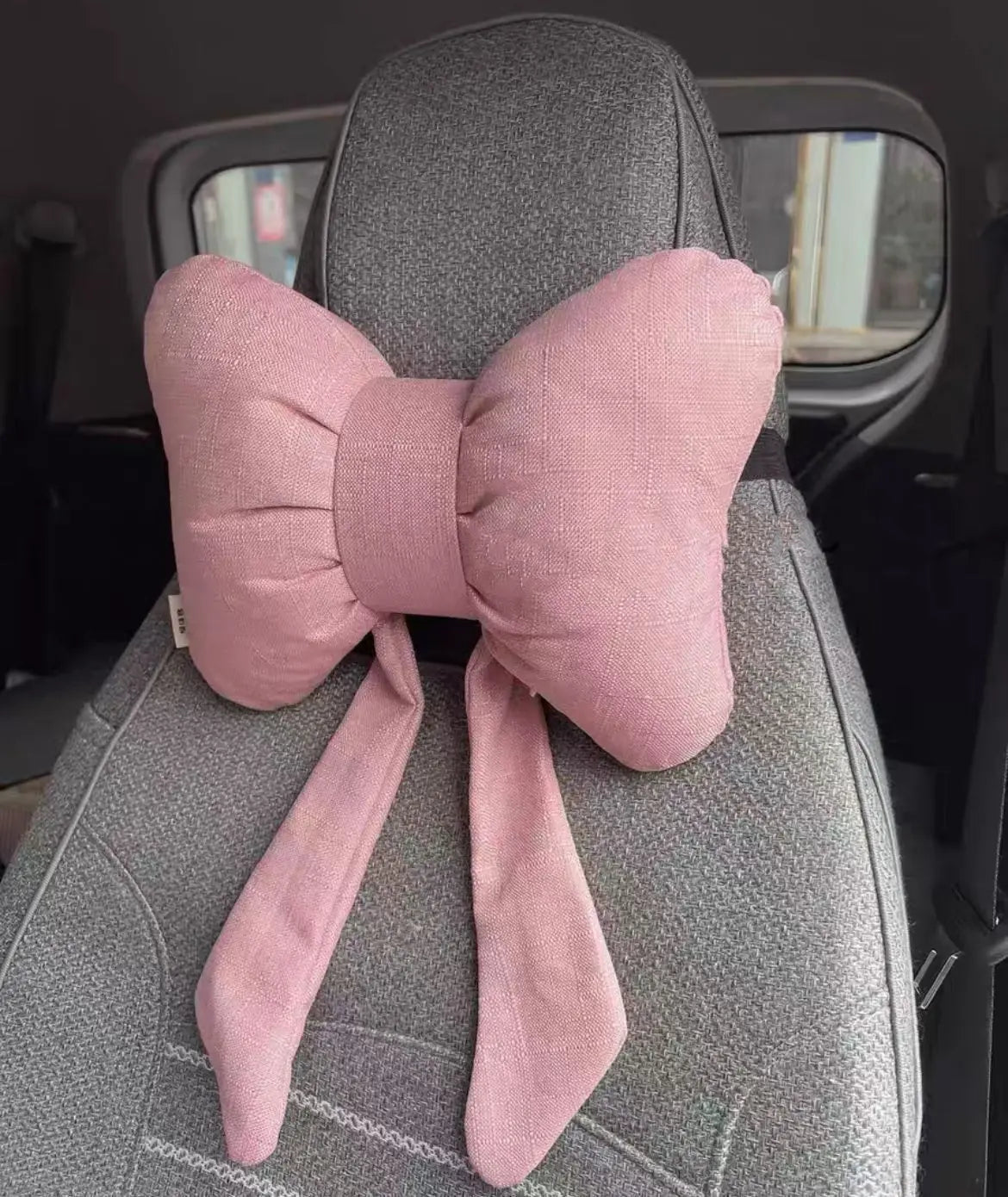 Oreiller de cou accent couleur papillon rose avec un nœud autour de l'appui-tête d'un siège auto.