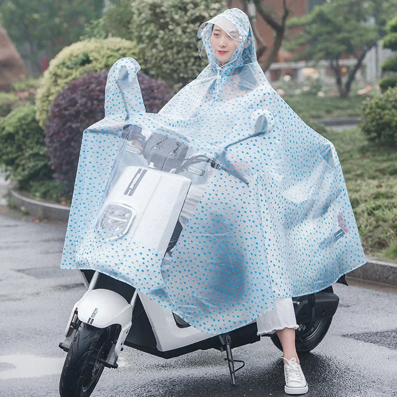 A woman wearing a transparent blue polka-dot windproof motorcycle rain poncho while sitting on a white scooter.
