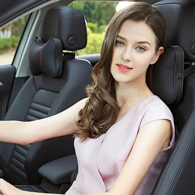 A young woman sits in a car seat, wearing a light pink top, with the headrest and seatbelt pads visible.