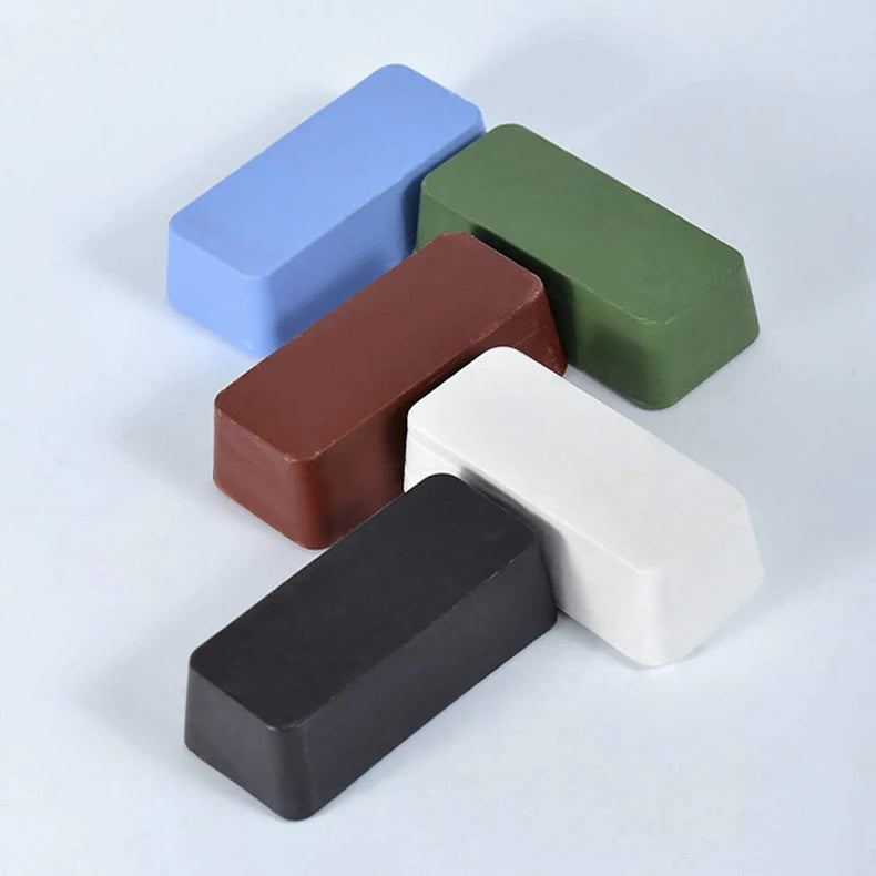 Six rectangular bars of metal polishing wax in blue, green, brown, white, and black are arranged on a white surface.