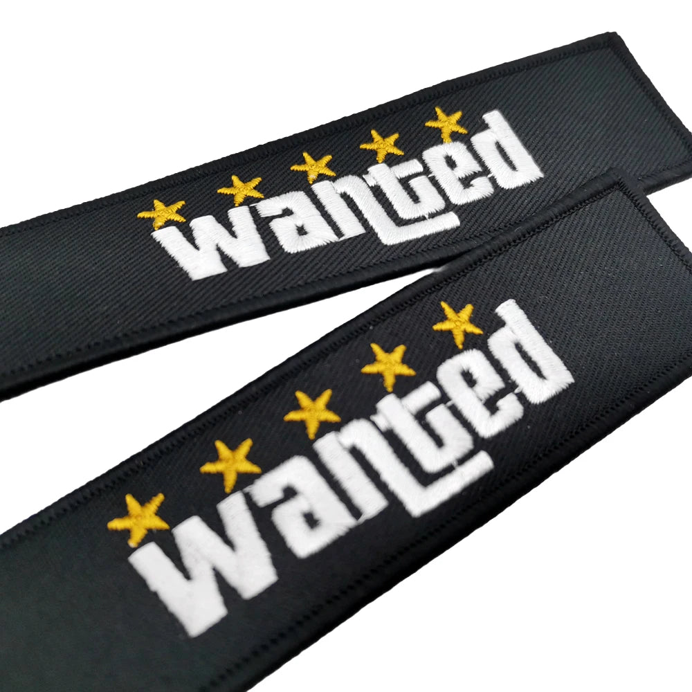 Porte-clés en nylon noir avec texte brodé blanc 'Wanted' et cinq étoiles jaunes