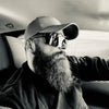 Un homme portant une casquette de baseball et des lunettes de soleil regarde par la vitre d'une voiture.