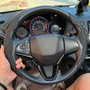 A hand is holding a black steering wheel of a car with a leather-wrapped rim and controls visible.