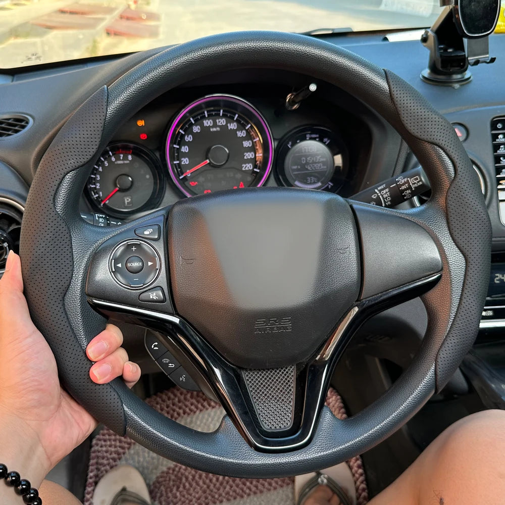 A hand is holding a black steering wheel of a car with a leather-wrapped rim and controls visible.