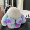 A fluffy plush bunny keychain featuring light blue and purple fur with a gold ring.