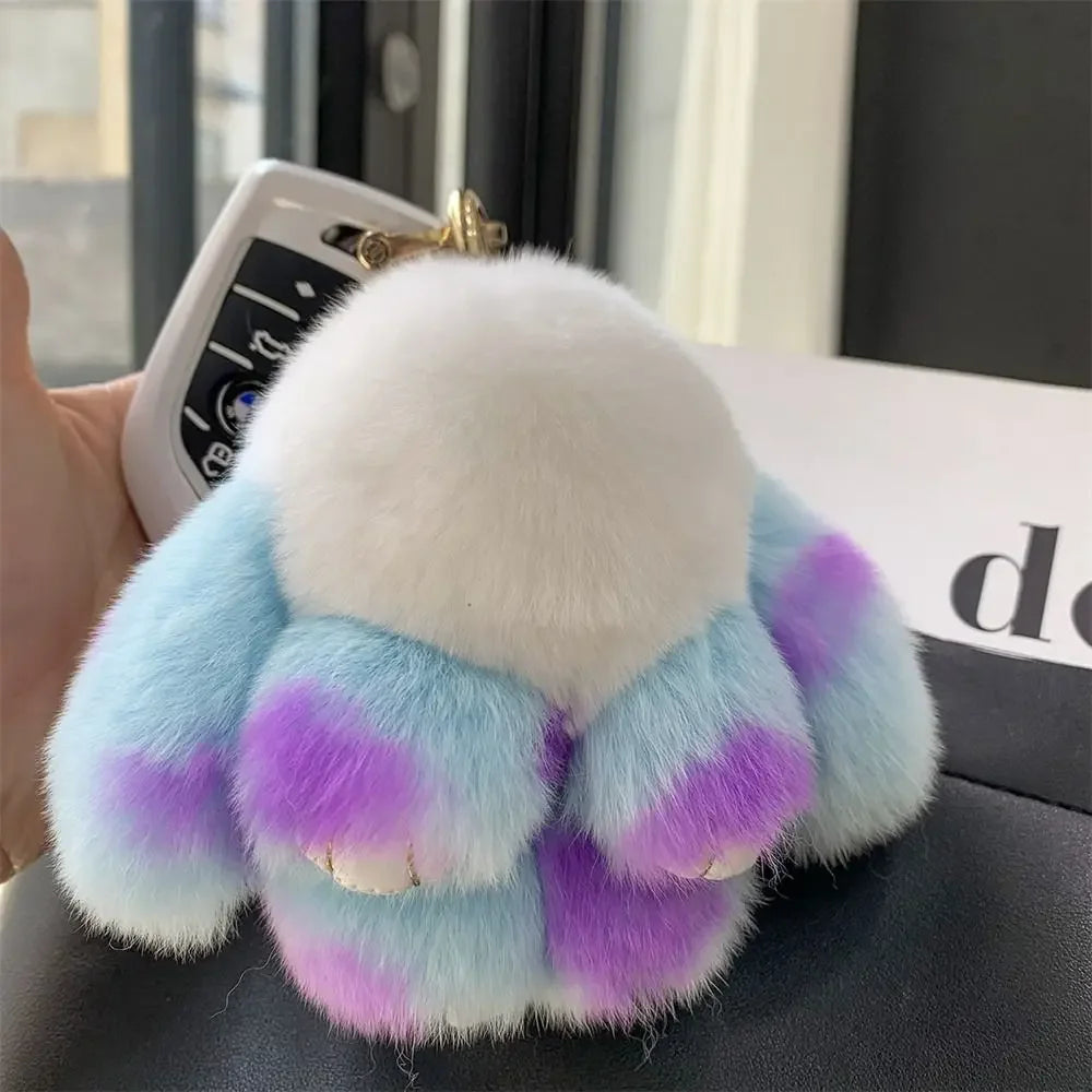 A fluffy plush bunny keychain featuring light blue and purple fur with a gold ring.