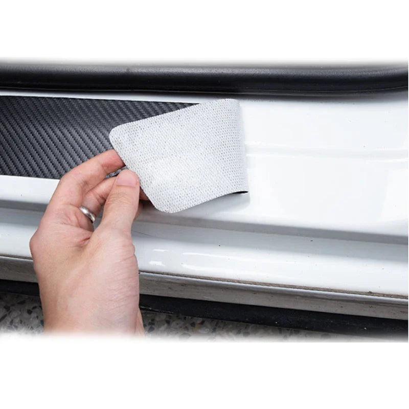 A hand is placing a white carbon fiber door sill protector onto a car door frame.
