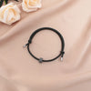 A black heart-shaped fitness tracker bracelet is displayed on a soft pink fabric with white roses.
