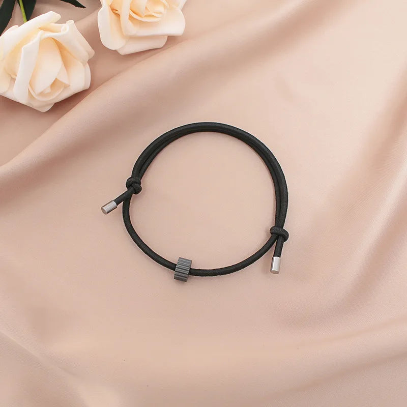 A black heart-shaped fitness tracker bracelet is displayed on a soft pink fabric with white roses.
