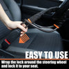 A hand is wrapping a black and orange strap around a steering wheel to secure it to a car seat.