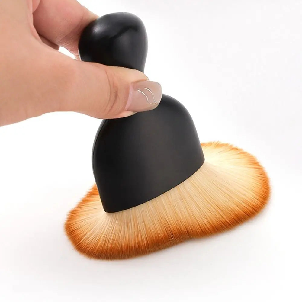A hand is holding a black curved silicone car interior cleaning brush with golden bristles.