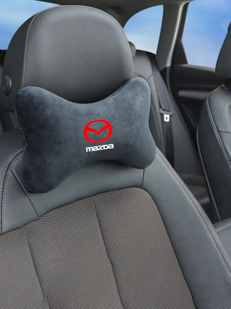 A close-up view of a black car headrest featuring a gray fabric shoulder pad with the Mazda logo.