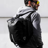 A man wearing a grey hoodie and black pants is carrying a black foldable waterproof bike pannier bag.