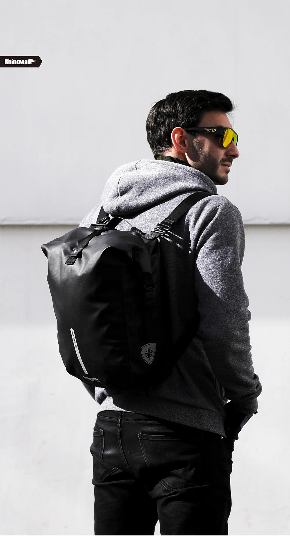 A man wearing a grey hoodie and black pants is carrying a black foldable waterproof bike pannier bag.