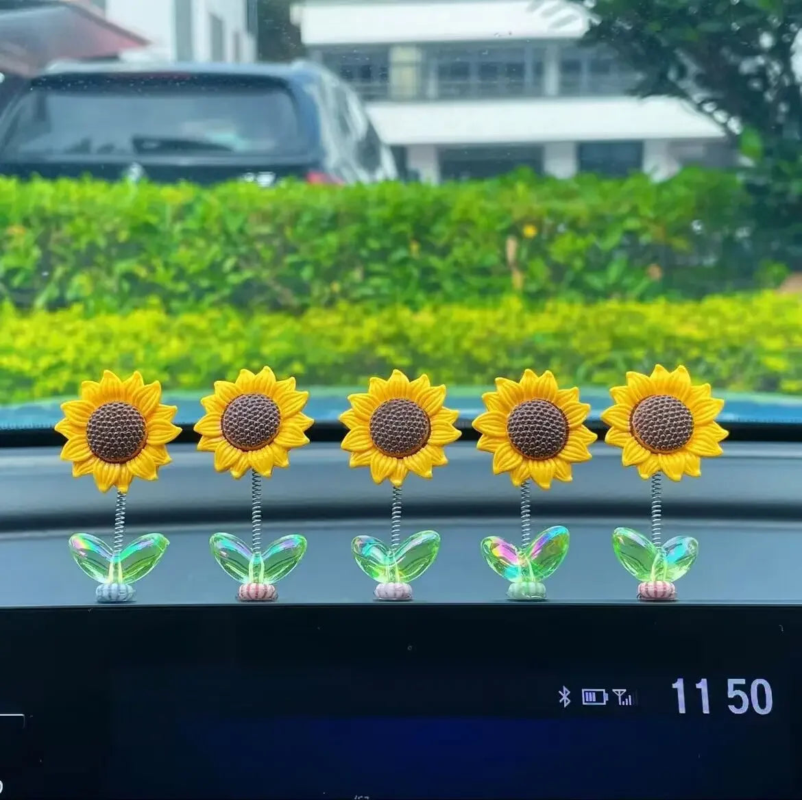 Ornements de voiture en forme de tournesol jaune avec des tiges vertes, exposés sur une console sombre.
