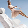 A woman in a light pink dress is shown leaping over white ergonomic lumbar and neck pillows.