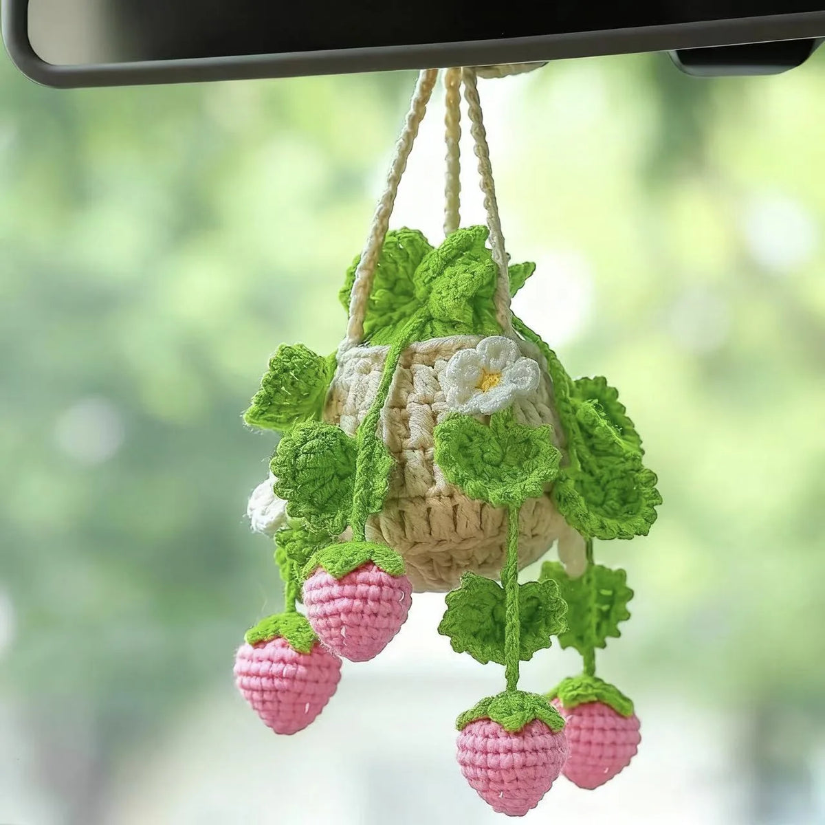 A crochet hanging strawberry decor made of green leaves and pink strawberries, suspended by twine.