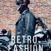 A person wearing a black leather jacket and a retro half helmet stands in front of motorcycles.