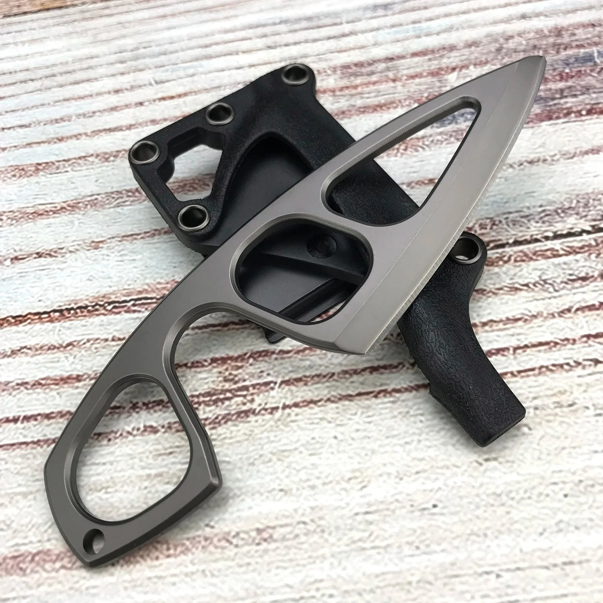 A gray fixed blade knife is shown with a black sheath, resting on a light wooden surface.