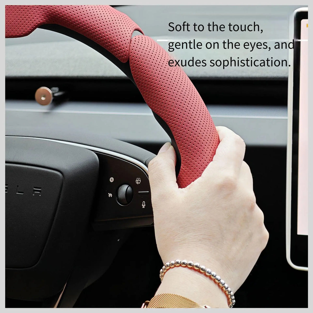 A hand is gripping a reddish-pink perforated leather steering wheel cover on a car interior.