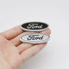 Eine Hand hält zwei ovale Ford-Lenkrad-Zieraufkleber, einer schwarz und einer silber.