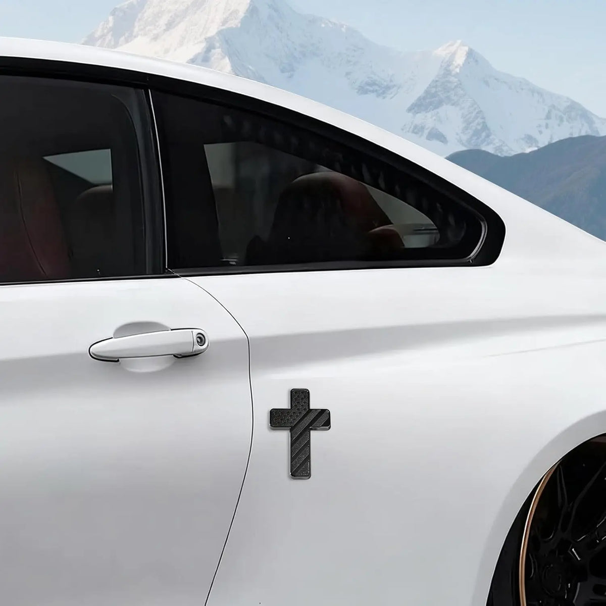 Ein weißes Auto mit einem schwarzen Kreuzaufkleber auf der Tür vor einer Berglandschaft im Hintergrund.