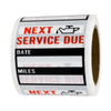 A roll of oil change reminder stickers with text indicating next service due, miles, and date.