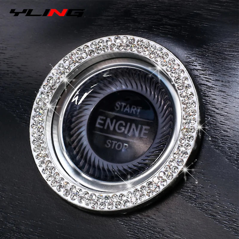 A close-up of a round, silver car start button cover decorated with clear diamond rhinestones.