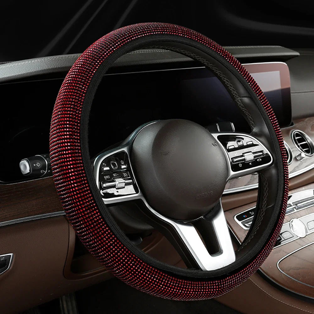 A close-up view of a black steering wheel with a red rhinestone cover inside a car interior.