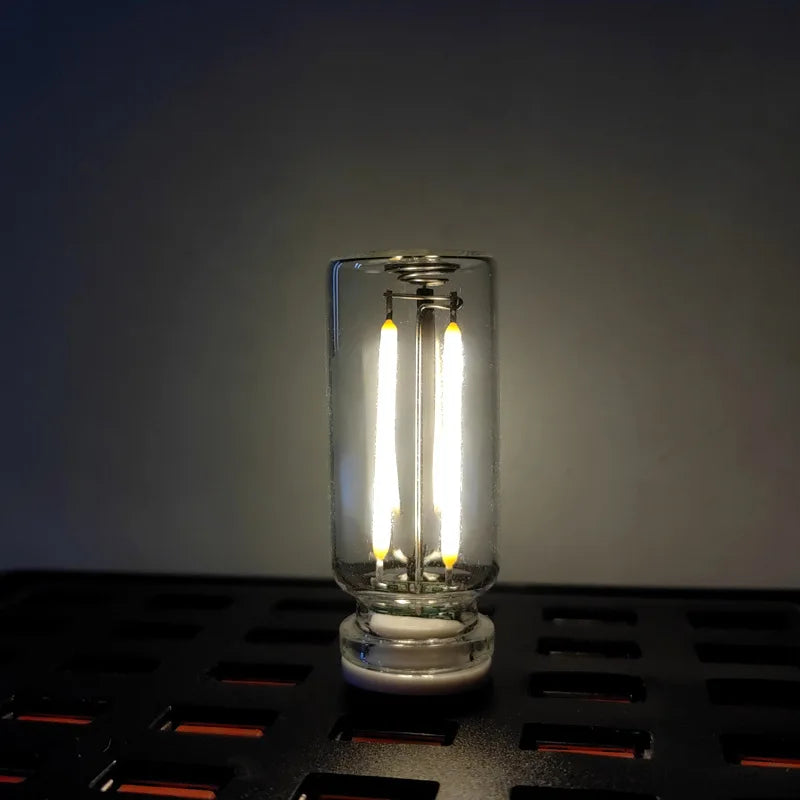 A clear glass LED night light with a filament bulb is displayed on a dark surface.