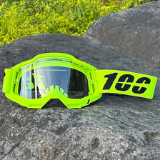 A pair of neon yellow sports goggles with a black lens resting on a dark gray rock.
