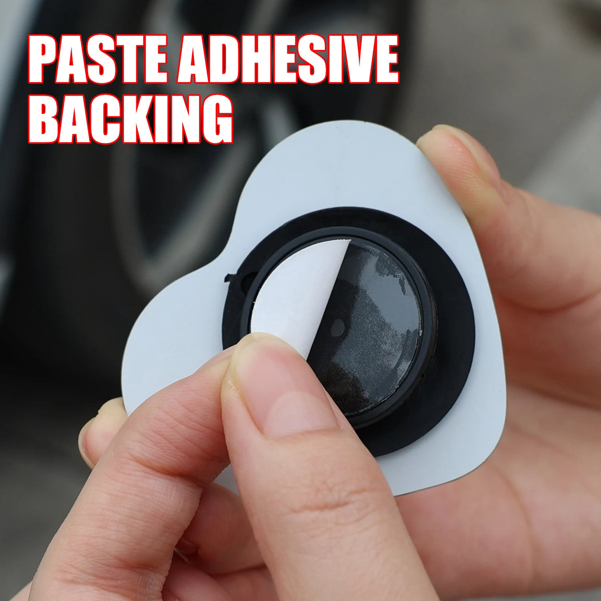 Une main tient un rétroviseur aveugle en forme de cœur blanc avec une lentille noire et un fond adhésif.