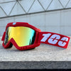 A pair of red windproof sports goggles with yellow-tinted lenses resting on a gray surface.