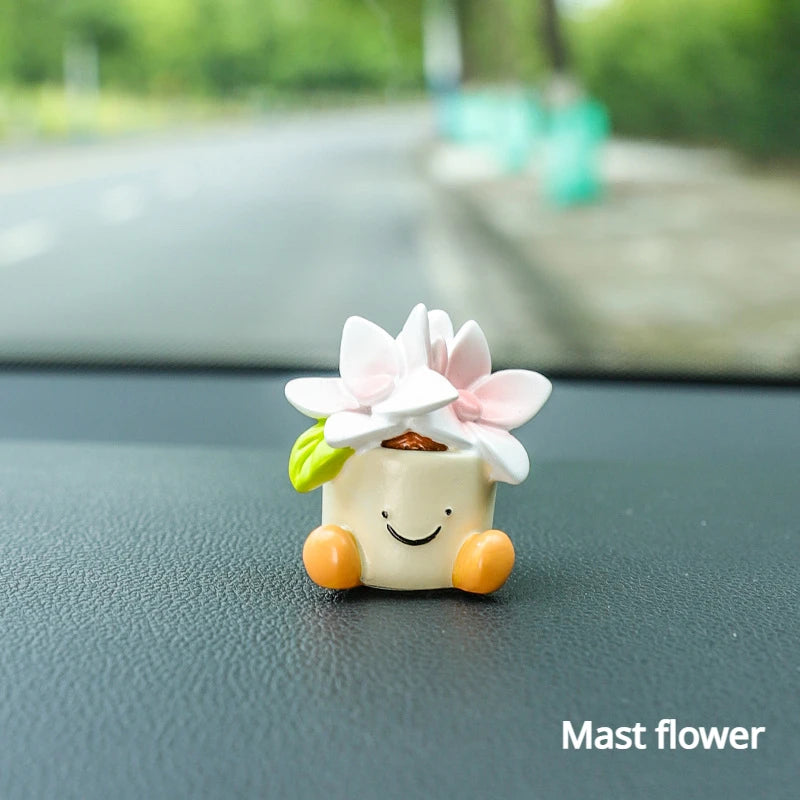 Kleine weiße Harzblumen-Topf Elfen-Auto-Dekoration mit rosa Blüten und grünen Blättern auf dunker Oberfläche.