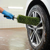 A hand using a heavy-duty wheel barrel brush to clean the rim of a car tire.