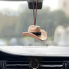 A tan cowboy hat ornament is hanging from a string above a car interior.