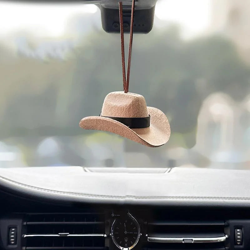 A tan cowboy hat ornament is hanging from a string above a car interior.