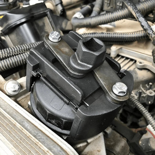 A black adjustable oil filter wrench with serrated jaws is shown in a close-up view against an engine component.