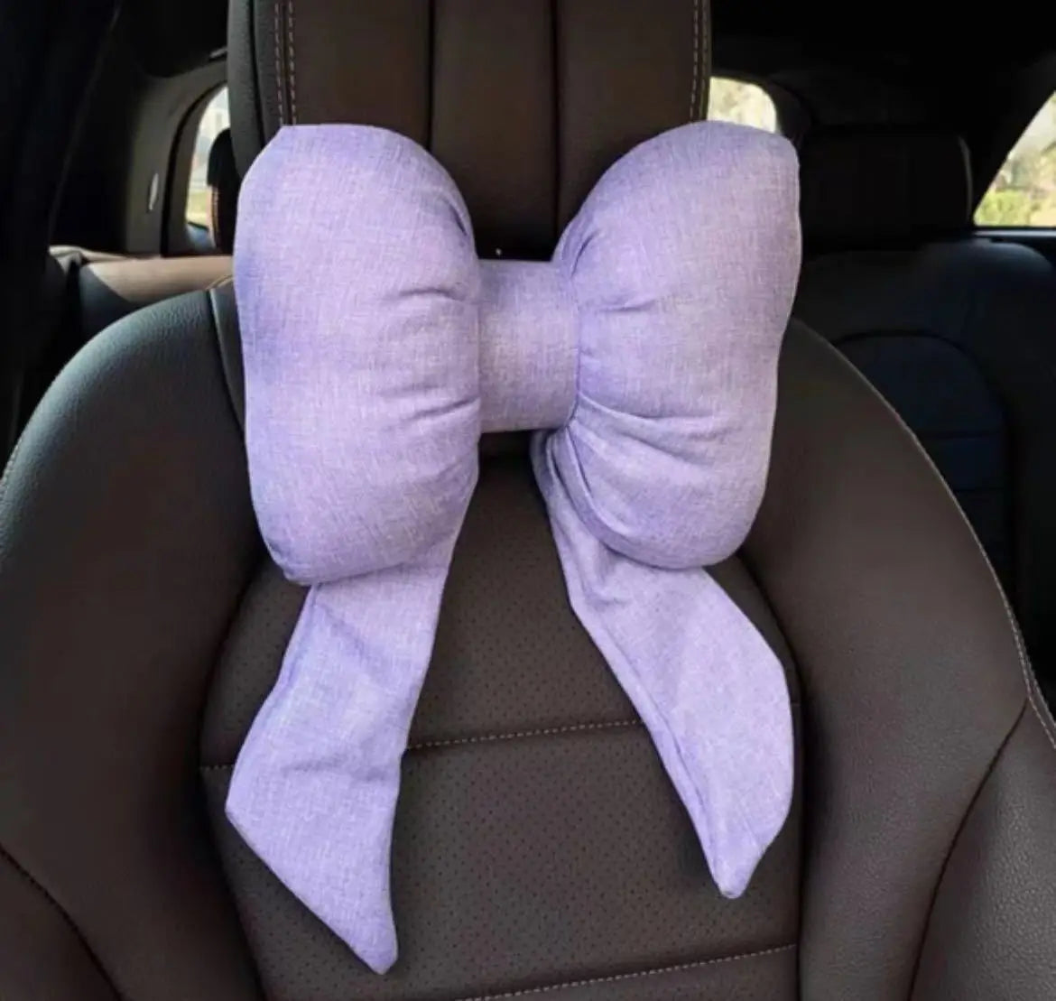 Oreiller de cou papillon en tissu violet clair noué, posé sur un siège de voiture sombre.