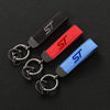 Three leather keychains featuring the letter S in black, red, and blue suede on a black background.