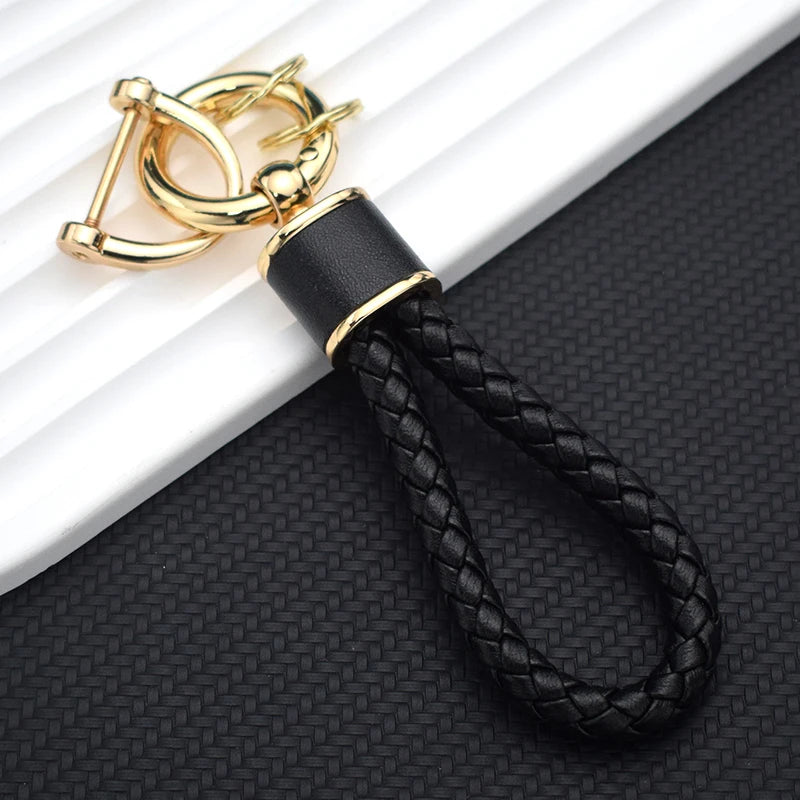 Gold-toned multi-function car key cover with a black braided strap resting on a white surface.