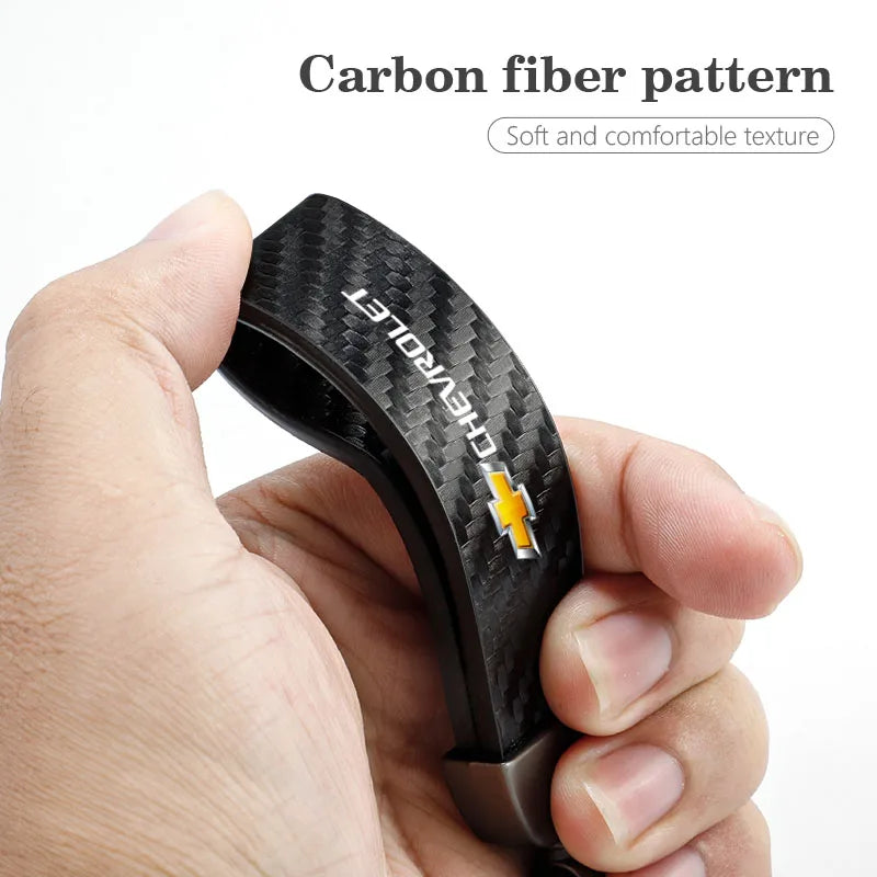 A hand holds a black carbon fiber pattern car key fob for a luxury metal keyring set.