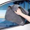 A hand is holding a gray multi-sided coral fleece drying towel against a glass window background.