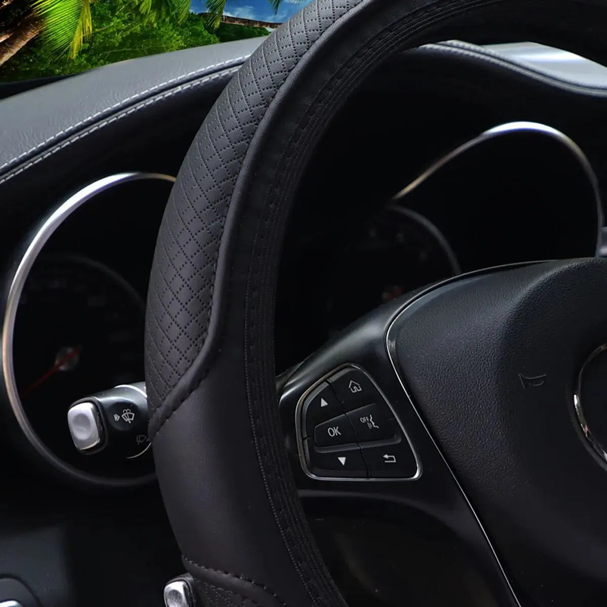 Close-up view of a black embossed leather steering wheel cover inside a car interior.