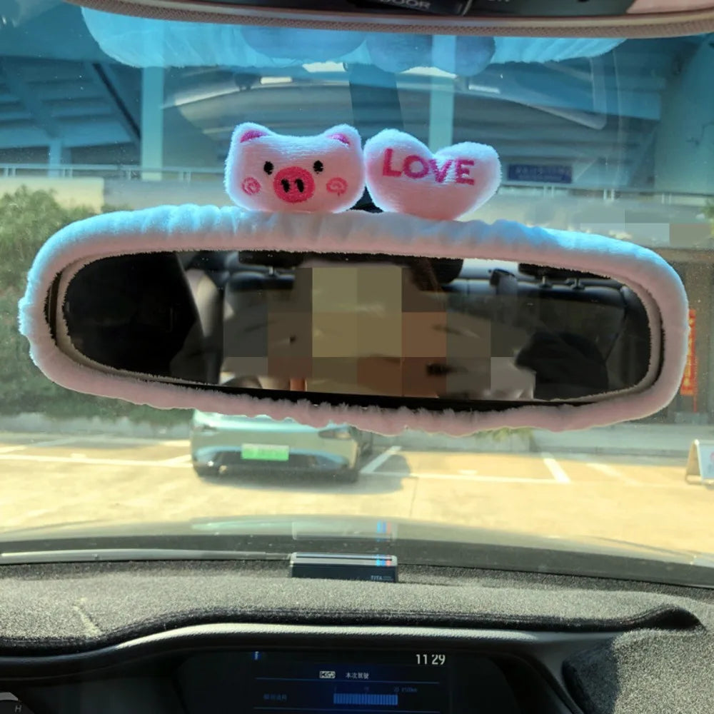 A pink plush heart shaped item with the word LOVE is placed on a car's rearview mirror.