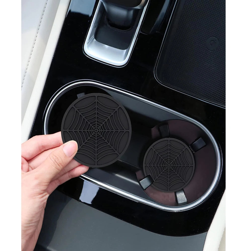 A hand is placing a silicone spider web coaster into a black car accessory tray.